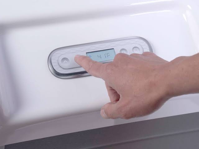 A close-up of a person’s hand pressing a button on the tub's integrated digital control panel. The LCD screen displays a temperature of 41 degrees Fahrenheit.